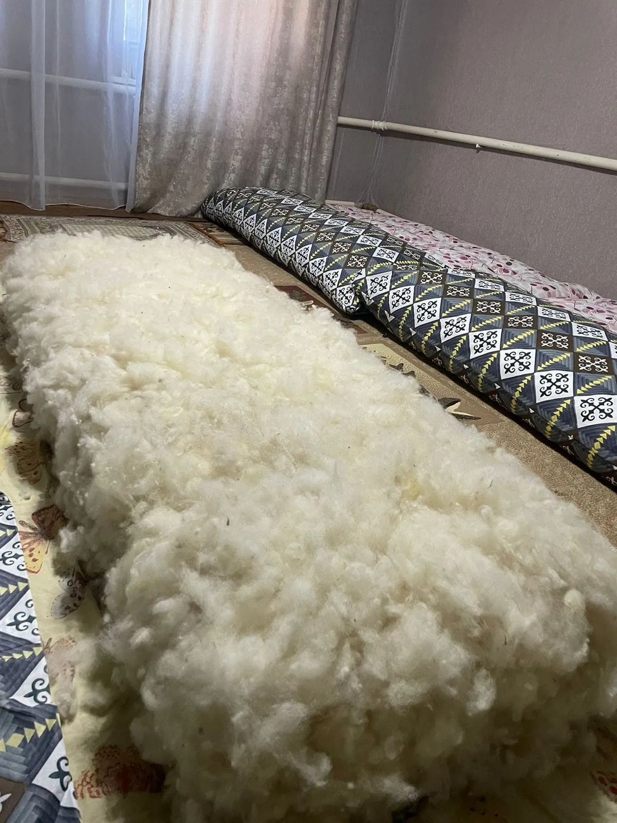 Белая овечья шерсть, разложенная на ткани перед набивкой корпе